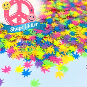 May include: A pile of colorful glitter in the shape of marijuana leaves. The glitter is a mix of neon green, pink, yellow, blue, and purple.