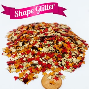 May include: A pile of gold, red, and orange glitter shaped like maple leaves. A US penny is included for scale.