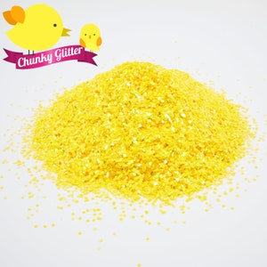 May include: A pile of bright yellow chunky glitter. The glitter is scattered on a white surface. The text "Chunky Glitter" is written on a pink ribbon.