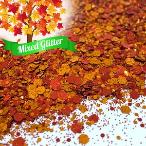 May include: A close-up of a mix of red, orange, and gold glitter. The glitter is in the shape of small hexagons and circles. The glitter is scattered on a white surface. The text "Mixed Glitter" is on a green ribbon.