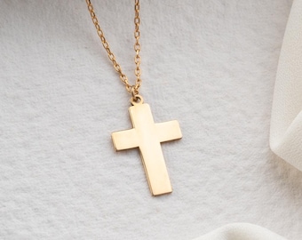 May include: A gold chain necklace with a simple gold cross pendant. The necklace is laying on a white fabric background.