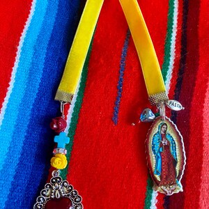 May include: Two yellow velvet ribbon bookmarks with charms. One bookmark has a silver heart charm with a red stone and the other has a silver charm with a picture of the Virgin Mary and the word "Faith".