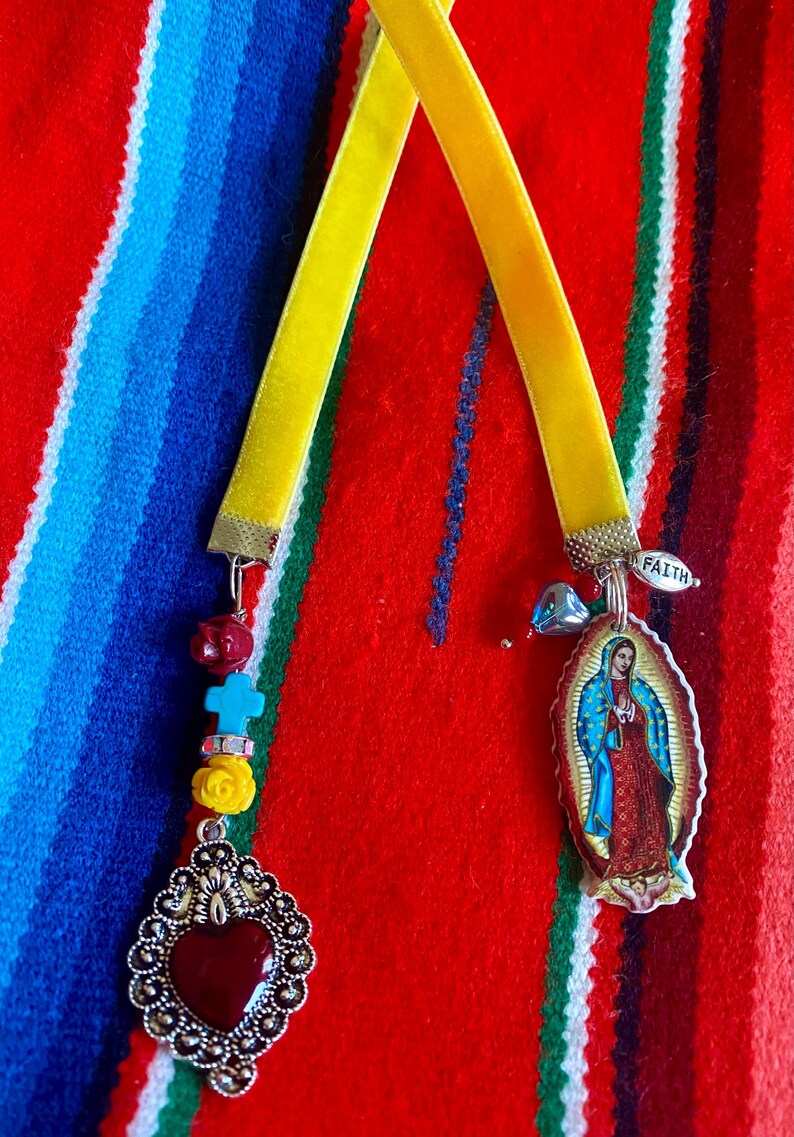 May include: Two yellow velvet ribbon bookmarks with charms. One bookmark has a silver heart charm with a red stone and the other has a silver charm with a picture of the Virgin Mary and the word "Faith".