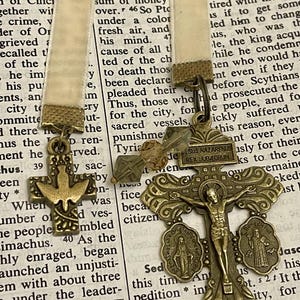 Pu&ograve; includere: Un ciondolo a forma di croce dorata con una figura di Ges&ugrave; Cristo sulla croce. La croce &egrave; decorata con dettagli intricati e ha un piccolo ciondolo rotondo con una rappresentazione della Vergine Maria sul lato sinistro. La croce &egrave; appesa a un nastro con un piccolo ciondolo a forma di ancora dorato.