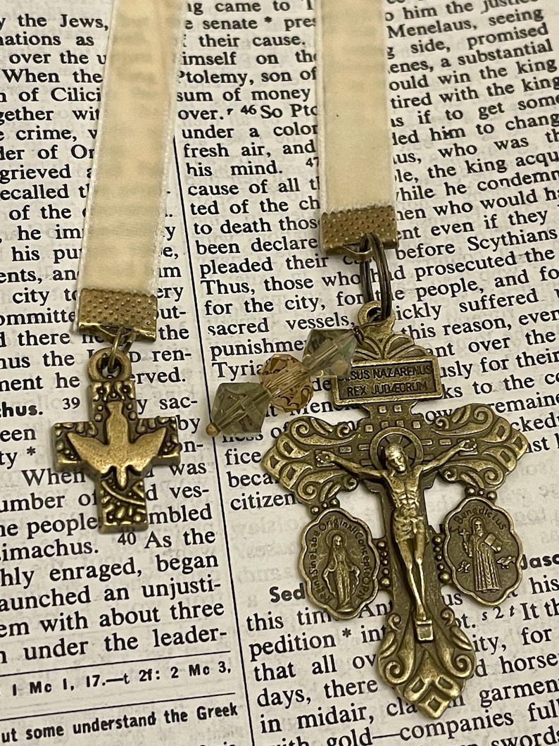 Pu&ograve; includere: Un ciondolo a forma di croce dorata con una figura di Ges&ugrave; Cristo sulla croce. La croce &egrave; decorata con dettagli intricati e ha un piccolo ciondolo rotondo con una rappresentazione della Vergine Maria sul lato sinistro. La croce &egrave; appesa a un nastro con un piccolo ciondolo a forma di ancora dorato.