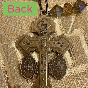 Pu&ograve; includere: Un ciondolo a forma di croce di colore bronzo con le parole "Behold this heart which has so loved men" e "Forgive them" sul davanti. Il retro del ciondolo ha le parole "Father" e un piccolo ciondolo rotondo con le parole "Pax Vobis" e una croce.