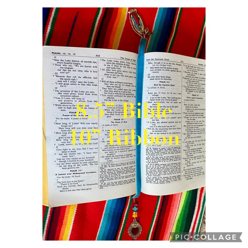 May include: An open Bible with a blue ribbon bookmark. The bookmark has a heart-shaped charm with beads. The Bible pages are open to Psalms 13, 14, and 15.