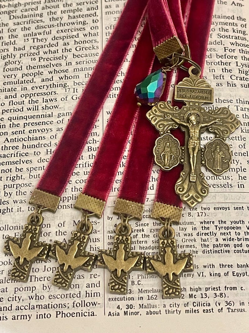 Pu&ograve; includere: Un segnalibro in nastro di velluto rosso con un ciondolo a forma di croce in metallo dorato che presenta una figura di Ges&ugrave; Cristo. La croce &egrave; decorata con tre medaglioni pi&ugrave; piccoli e un cristallo iridescente scintillante. Il segnalibro &egrave; perfetto per aggiungere un tocco di fede ed eleganza alla tua esperienza di lettura.