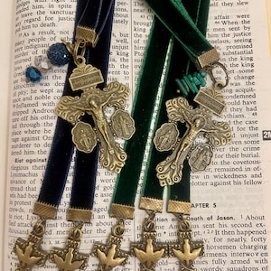 Pu&ograve; includere: Tre segnalibri dorati con un tema religioso. Ogni segnalibro presenta una croce con una colomba e le parole "Jesus Nazarenus Rex Iudeorum" sulla croce. I segnalibri sono attaccati a nastri di velluto blu e verde.