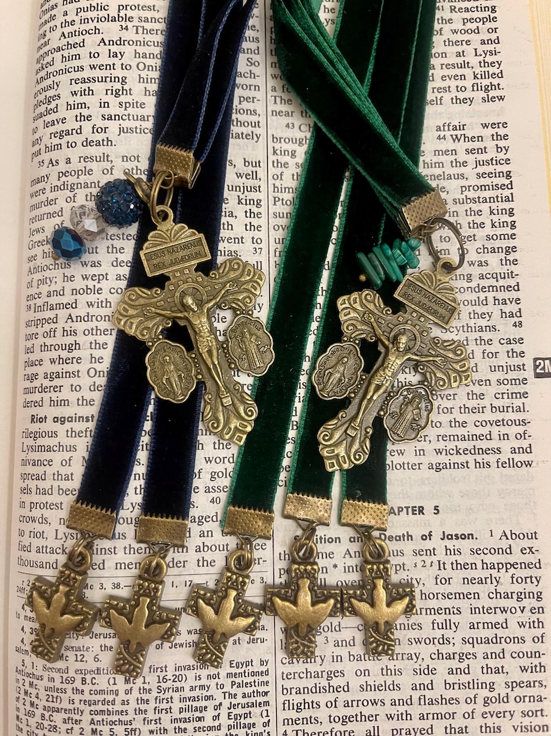 Pu&ograve; includere: Tre segnalibri dorati con un tema religioso. Ogni segnalibro presenta una croce con una colomba e le parole "Jesus Nazarenus Rex Iudeorum" sulla croce. I segnalibri sono attaccati a nastri di velluto blu e verde.