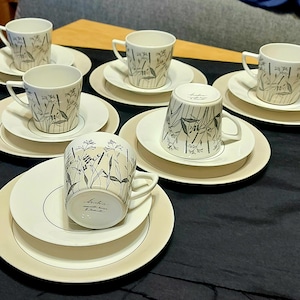 Puede incluir: Juego de seis tazas de té y platillos blancos con un patrón floral negro. Las tazas y los platillos tienen un diseño delicado y elegante.