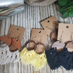 May include: Three pairs of earrings with wooden circles and fringe. The fringe is white, yellow, and black. The earrings are displayed on brown card stock.
