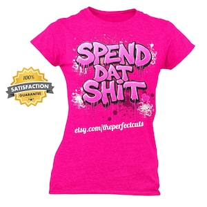May include: A bright pink short-sleeved t-shirt featuring the text SPEND DAT SHIT in a graffiti-style font with paint splatter effects. The shirt includes the website text etsy.com/theperfectcuts printed in white below the main graphic design.
