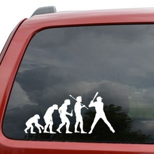 May include: A white vinyl decal of the evolution of man, ending with a baseball player swinging a bat. The decal is on the back window of a red car.
