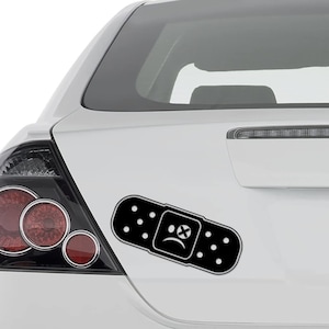 May include: Black and white car sticker of a band-aid with a sad face and an X over it.