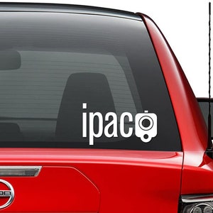 May include: White vinyl decal with the text "ipac" and a camera icon. The decal is on the back window of a red car.