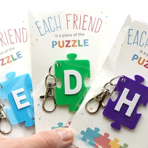 May include: Keychains shaped like puzzle pieces in blue, green, and purple, each with a different white letter. The keychains are packaged with cards that read "Each friend is a piece of the puzzle."
