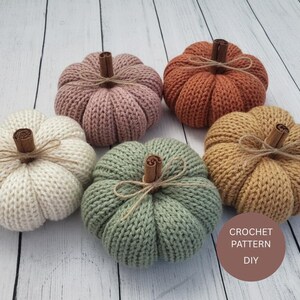 Puede incluir: Cinco calabazas hechas a mano con ganchillo en varios colores: blanco, rosa, naranja, verde y beige. Cada calabaza tiene un tallo de canela y un lazo de cuerda. Están dispuestas sobre una superficie de madera clara. El texto "CROCHET PATTERN DIY" es visible.