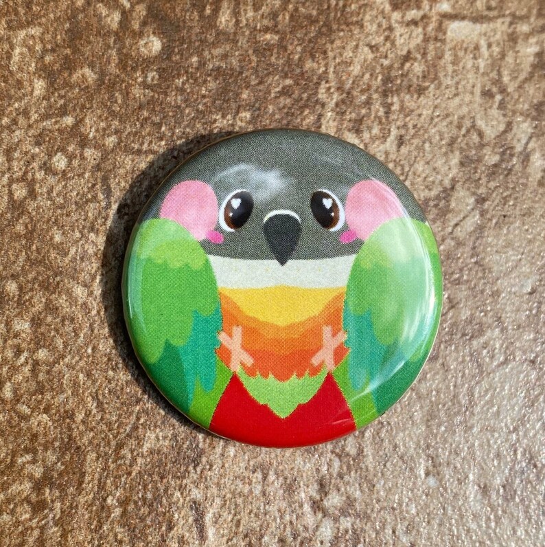 May include: A circular badge with a cartoon bird design. The bird has a grey head, green wings, and a red, orange, and yellow chest. The badge is set against a brown, textured background.