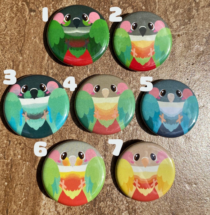 May include: Seven circular buttons with cartoon parrot designs. Each button showcases a different parrot with colours like green, blue, yellow, and red. The buttons are displayed on a brown surface.