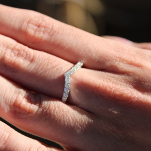 May include: A delicate, V-shaped ring with a row of sparkling diamonds set in a silver band.