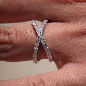 May include: A silver ring with a criss-cross design set with small clear stones.