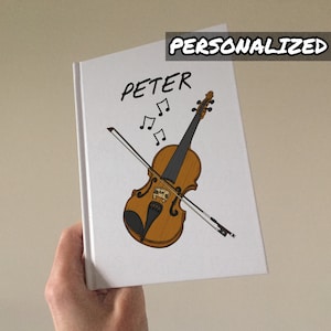 May include: White notebook with a violin illustration and the name "PETER" in black. The word "PERSONALIZED" is at the top. The violin is brown with a black fingerboard and bow. Musical notes are above the violin.