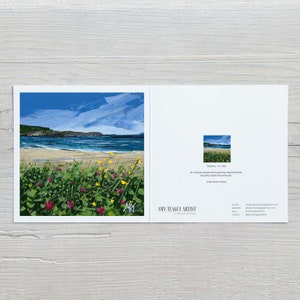 an image of a card lying down on a light wooden work top, the card has an image of a beach with yellow and pink flowers.