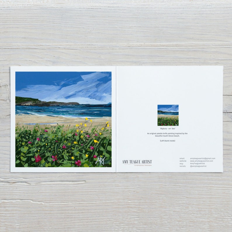 an image of a card lying down on a light wooden work top, the card has an image of a beach with yellow and pink flowers.