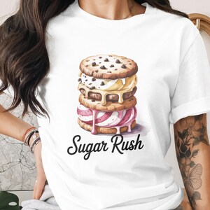 May include: White t-shirt featuring a watercolor illustration of a stack of ice cream sandwiches. The top cookie has chocolate chips. The text "Sugar Rush" is written in a script font below the ice cream sandwiches.