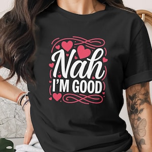 Peut inclure: T-shirt noir avec l'inscription "Nah I'm Good" en blanc, ornée de cœurs roses et de volutes décoratives. Un t-shirt décontracté pour un usage quotidien, au design simple et élégant.