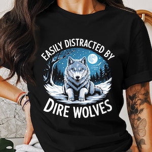 May include: Black t-shirt with a white dire wolf graphic and the text "Easily Distracted By Dire Wolves".