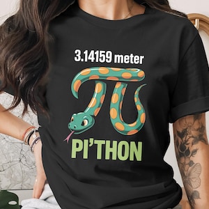 May include: Black t-shirt with a cartoon snake in the shape of the Pi symbol. The snake is green with orange spots and a pink tongue. The text "3.14159 meter" and "Pi'thon" are above and below the snake.