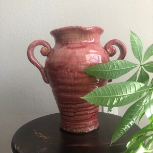 May include: A pink ceramic vase with two handles. The vase has a textured, slightly rippled surface and a glossy finish.