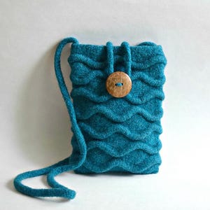 May include: Teal felted pouch with a wavy design and a wooden button closure. The small bag has a long, teal cord strap. The felted texture and unique design make this a stylish accessory. The pouch is approximately 15 cm tall and 10 cm wide.