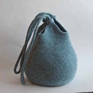 May include: A blue-grey felt drawstring bag with a rounded shape. The bag has a cinched top with a knotted closure and long, matching cord handles. The felt material appears soft and textured.