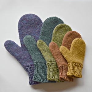 May include: A selection of knitted mittens in a range of sizes and colours. The mittens are in shades of purple, green, brown, and yellow. Each mitten has a ribbed cuff. The mittens are arranged on a white surface.