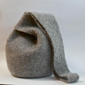 以下が含まれることがあります： 丸みを帯びたボディと長く尖ったフラップが付いた灰色のフェルトハット。帽子は柔らかく、質感のある素材で作られており、おそらく手作りです。帽子は無地の灰色で、コスチュームや普段使いに適しています。