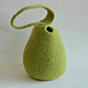 Könnte beinhalten: Eine birnenförmige Vase aus grünem Filz mit Schlaufengriff. Die Vase hat eine runde Öffnung oben und eine strukturierte Oberfläche. Der Griff ist mit einer kleinen goldfarbenen Öse befestigt.