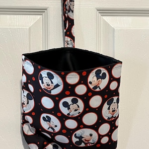 May include: A black and red fabric hanging storage bag featuring a pattern of Mickey Mouse in white circles. The bag has a black interior and a matching strap for hanging. The background is a white door.