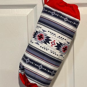May include: A fabric stocking with a Southwestern pattern in white, navy, red, and gray. The top and bottom are red, and a red ribbon is attached for hanging. The stocking is hanging on a white door.