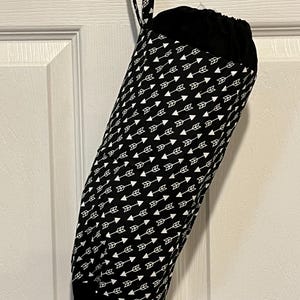 May include: A black and white fabric bag with a drawstring closure, hanging from a door. The bag is cylindrical and patterned with white arrows on a black background. The top and bottom are solid black.