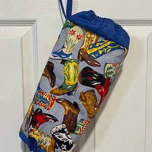 May include: A fabric storage bag with a blue drawstring top and a blue loop for hanging. The bag is patterned with various colorful cowboy boots on a light blue background.