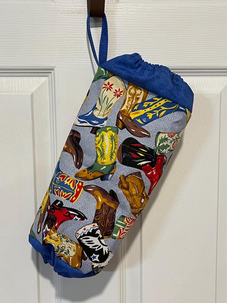 May include: A fabric storage bag with a blue drawstring top and a blue loop for hanging. The bag is patterned with various colorful cowboy boots on a light blue background.