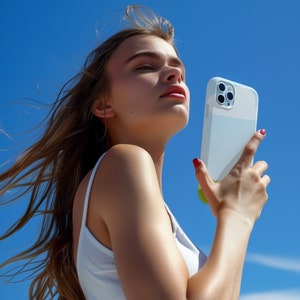 Op de afbeelding: Een vrouw met lang blond haar houdt een witte telefoonhoes met een uitsparing voor de camera lens. De hoes heeft een lichtblauw en groen ontwerp.