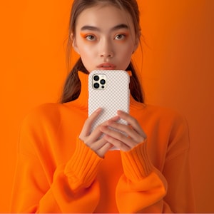 May include: A person wearing an orange turtleneck sweater is holding a white iPhone case with a camera lens cutout. The case has a checkered pattern.