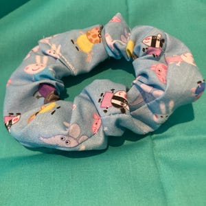 May include: A blue fabric scrunchie with a cartoon animal print. The scrunchie is made of soft, stretchy fabric and is perfect for holding hair in place.