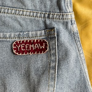 May include: A pair of light blue denim jeans with a red embroidered patch that says "YEEHAW" on the back pocket.