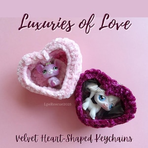 Puede incluir: Dos llaveros de terciopelo en forma de corazón con un pequeño animal de peluche dentro de cada uno. El llavero de la izquierda es rosa y el de la derecha es morado. El texto "Luxuries of Love" está en la parte superior de la imagen y el texto "Velvet Heart-Shaped Keychains" está en la parte inferior de la imagen.