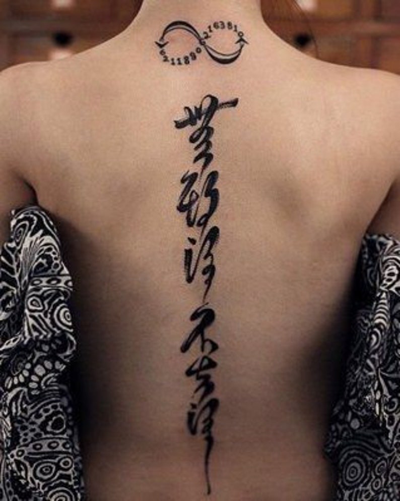 Puede incluir: Un tatuaje de tinta negra de una l&iacute;nea vertical de caligraf&iacute;a en la espalda de una persona. El tatuaje est&aacute; en la parte baja de la espalda y se extiende hasta el cuello. Hay un tatuaje m&aacute;s peque&ntilde;o de un s&iacute;mbolo de infinito con n&uacute;meros en el cuello.